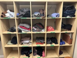 An open shelving unit with square sections holding Heather's clothes. Each box is labelled with green masking tape labels.